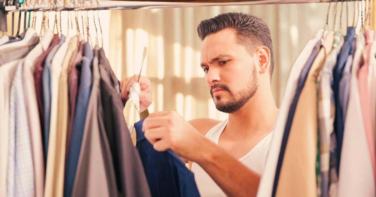 a man stands in front of his closet holding two shirts. he is wondering what to wear on a first date.