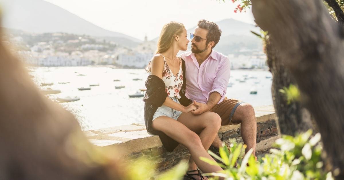 a man and woman look at each other romantically. they are outdoors, sitting by a body of water in the summertime. they have discovered the career benefits of a great relationship.