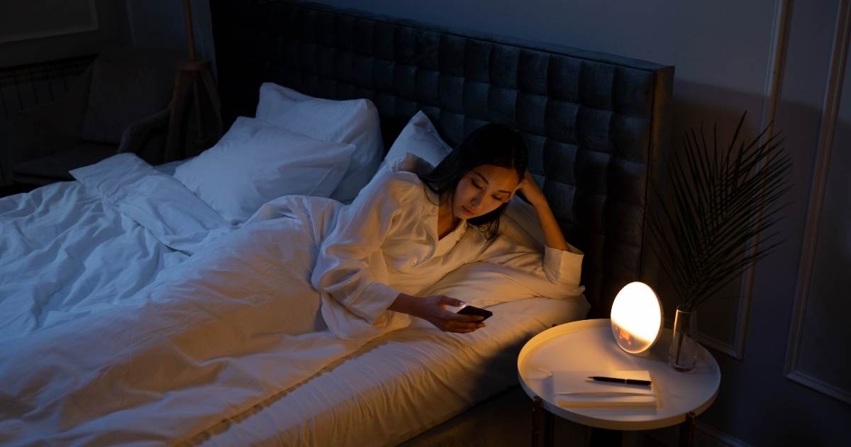 A woman lying in bed alone. She is using her phone to talk to ChatGPT about her relationship.