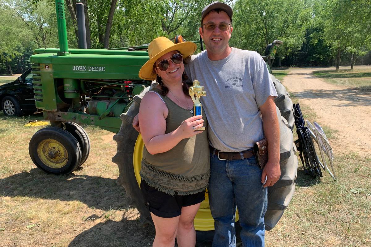Andrew and Elizabeth posing proudly with a trophy. They are outdoors on a sunny day, in a farm setting.