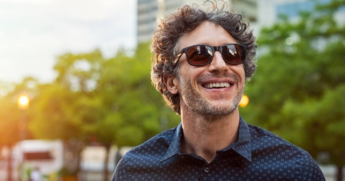 a confident man wearing sunglasses and smiling. he knows when to ask for help with dating.