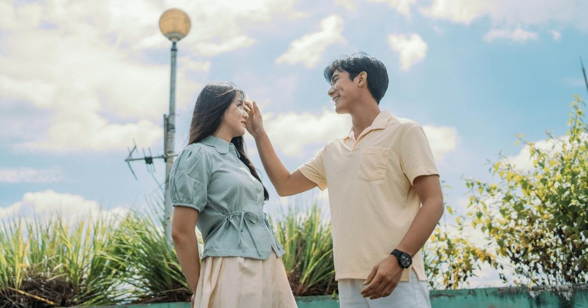 An idyllic couple looking sweetly at one another. Outdoors, clear blue sky. He is tucking her hair behind her ear. If you're asking, "Will I ever find love like this couple?", the answer is yes.