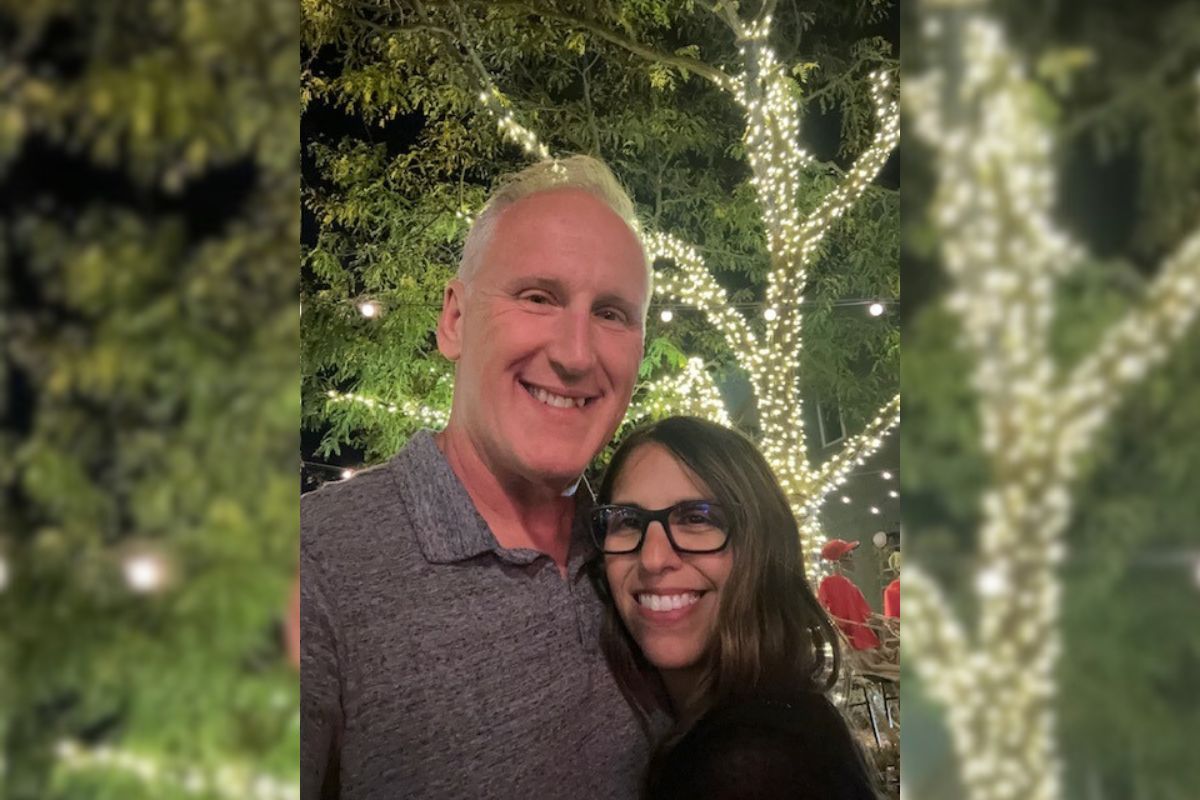 Mike and Jacquelyn posing for a selfie in front of a tree wrapped in twinkle lights.